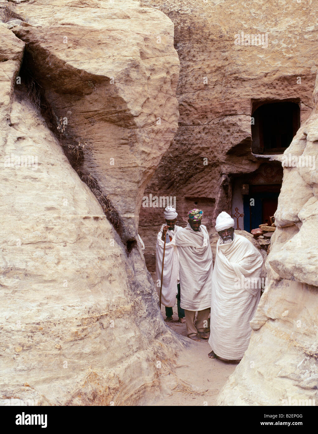 Priests of the Ethiopian Orthodox Church pause at the entrance to the rock-hewn church of Yohannes Maequddi. Stock Photo