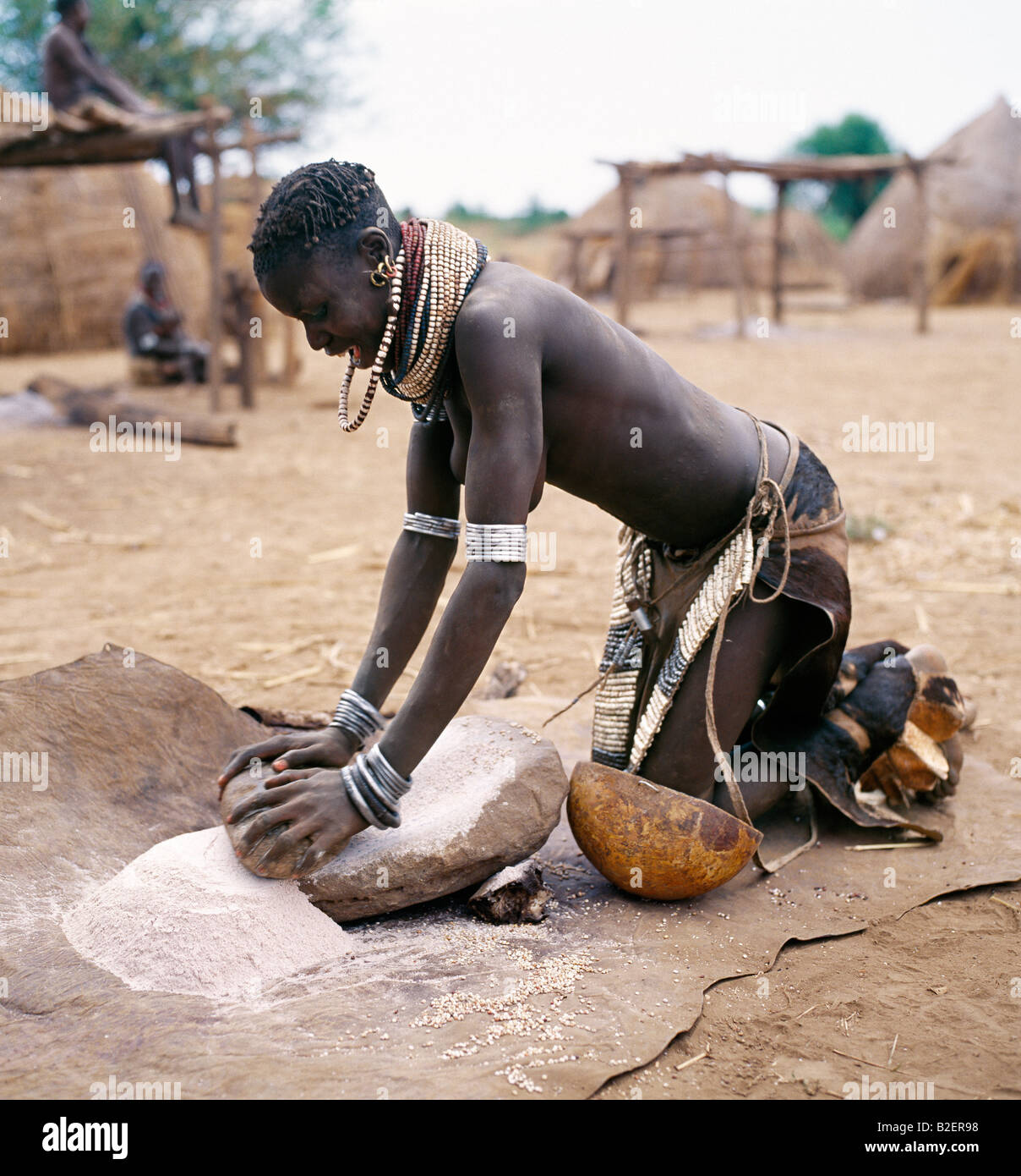 A Nyag'atom woman grinds sorghum using a flat stone. The Nyag'atom are one of the largest tribes and arguably the most warlike. Stock Photo