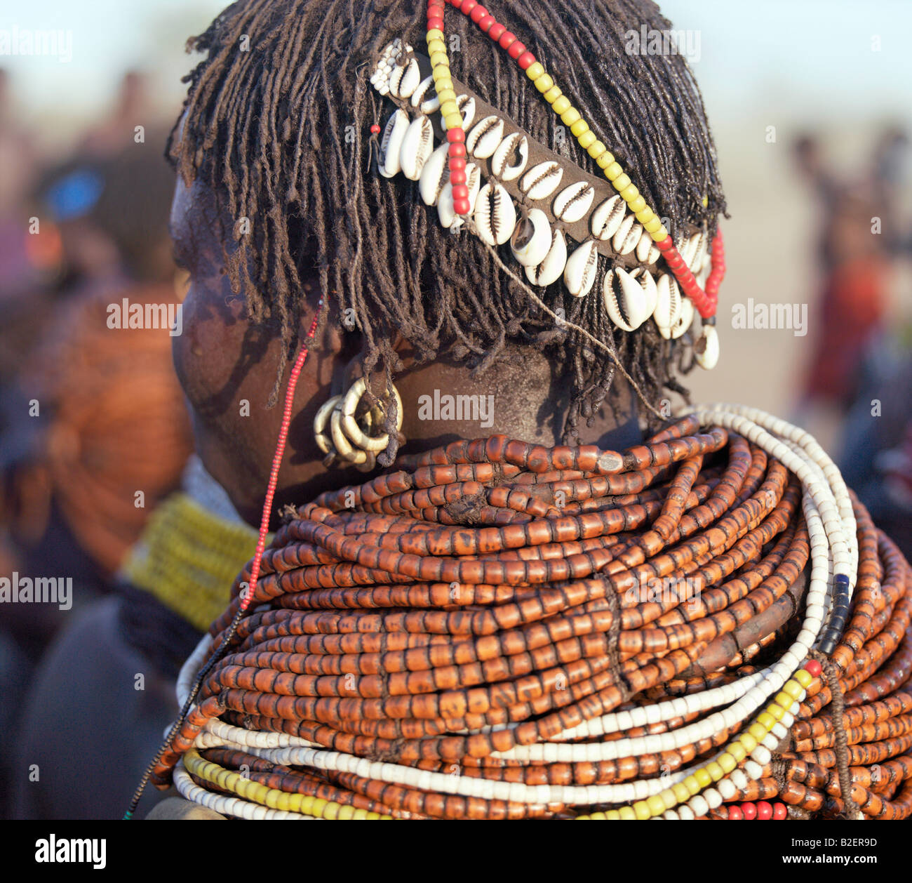 A Nyag'atom woman wears numerous strands of wooden beads and has decorated her braided hair with cowries backed onto leather. Stock Photo
