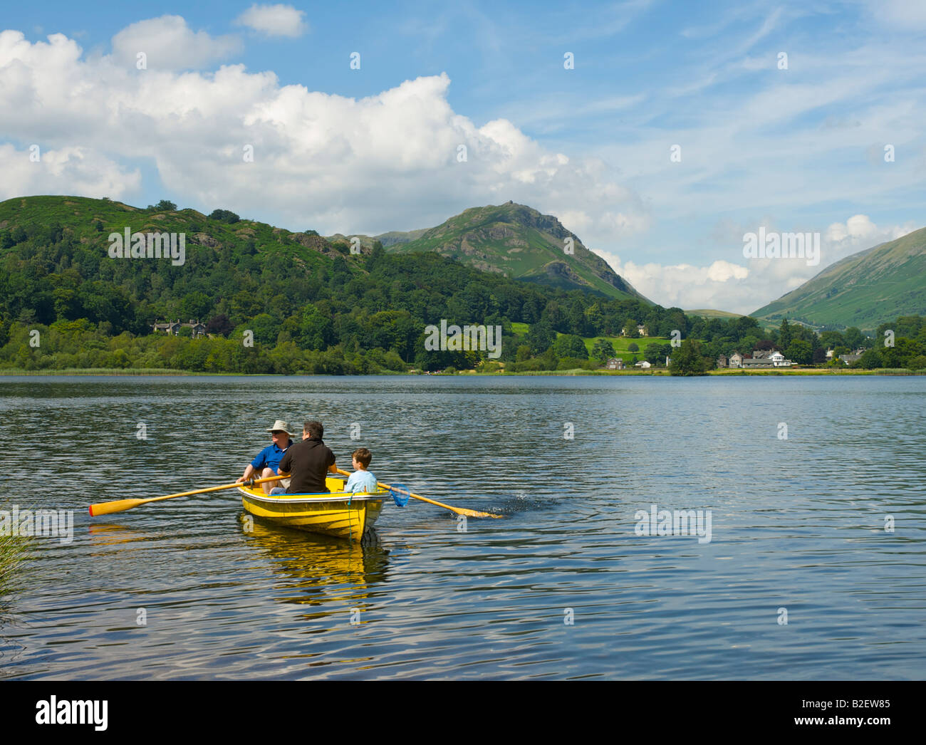 Three people in a yellow rowing boat on Grasmere, Lake District ...