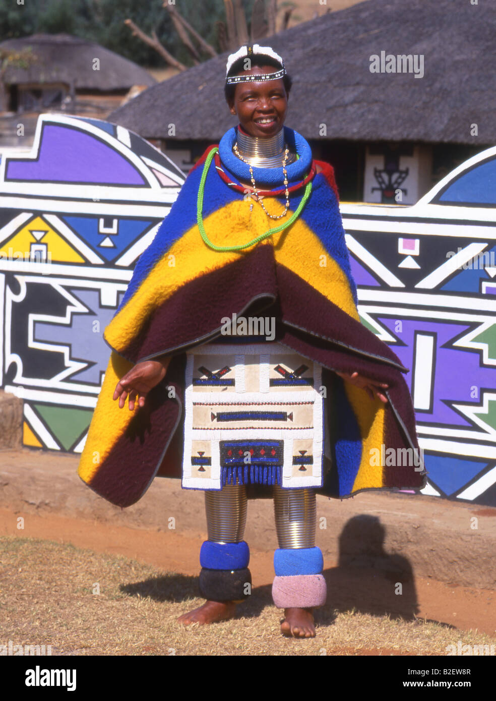 Ndebele Woman in traditional dress standing in front of traditionally painted house Stock Photo