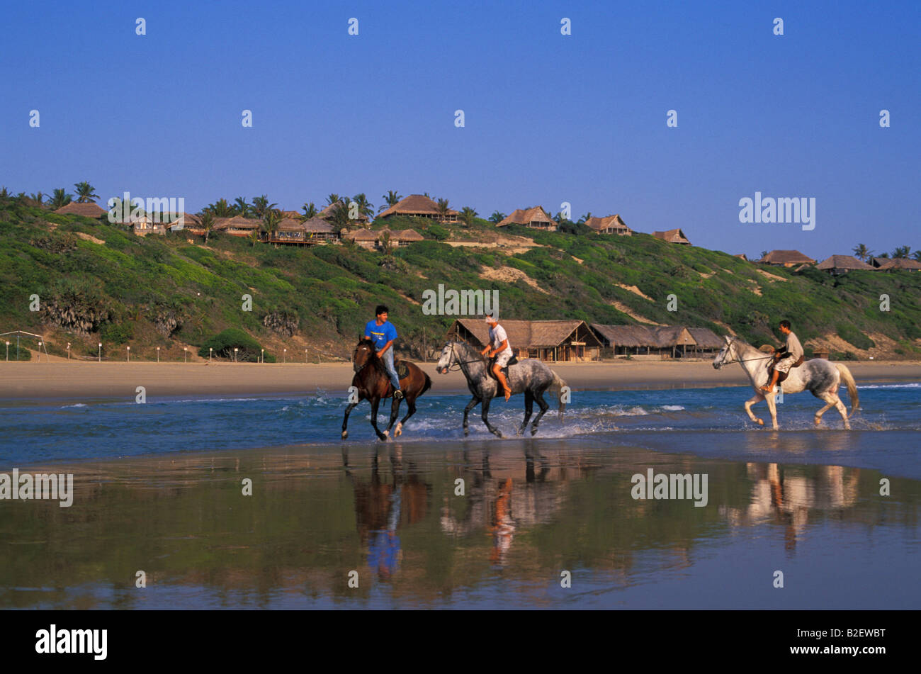 Tourists riding horses on the beach against the backdrop of thatched seaside cottages Stock Photo