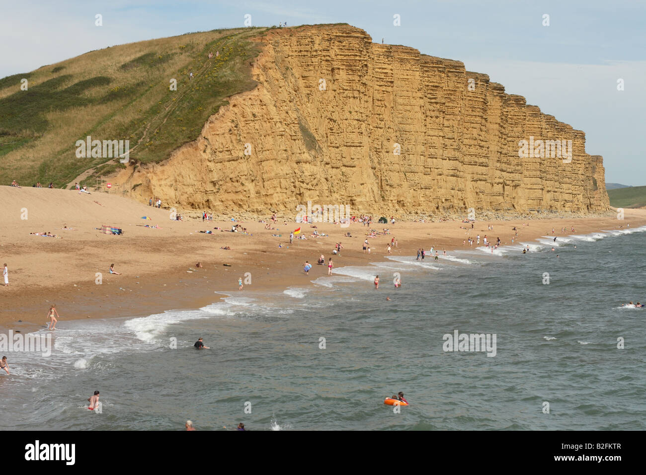 West Bay Dorset near Bridport the beach and East Cliff area in July with tourists on beach and swimming in the sea Stock Photo