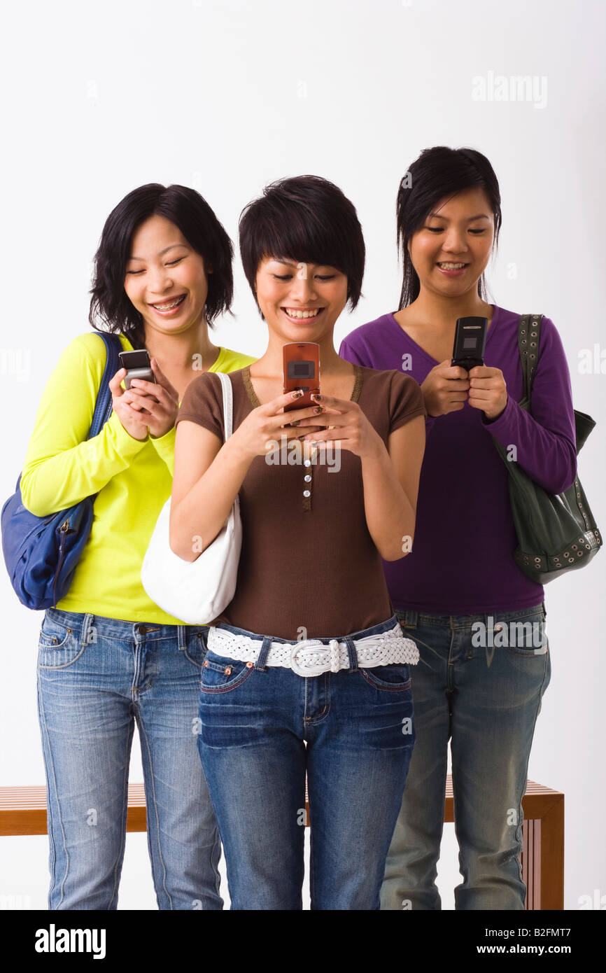Three young women using mobile phones and smiling Stock Photo - Alamy
