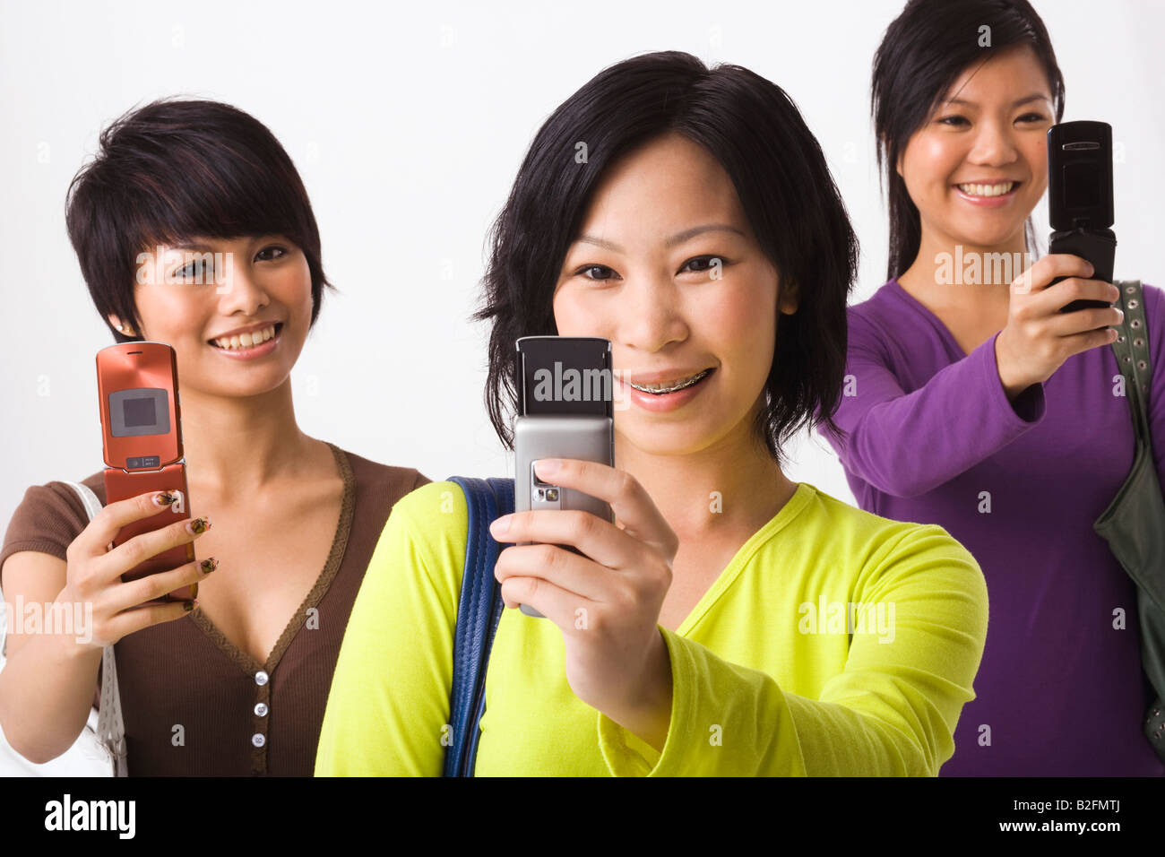Three young women using mobile phones and smiling Stock Photo - Alamy
