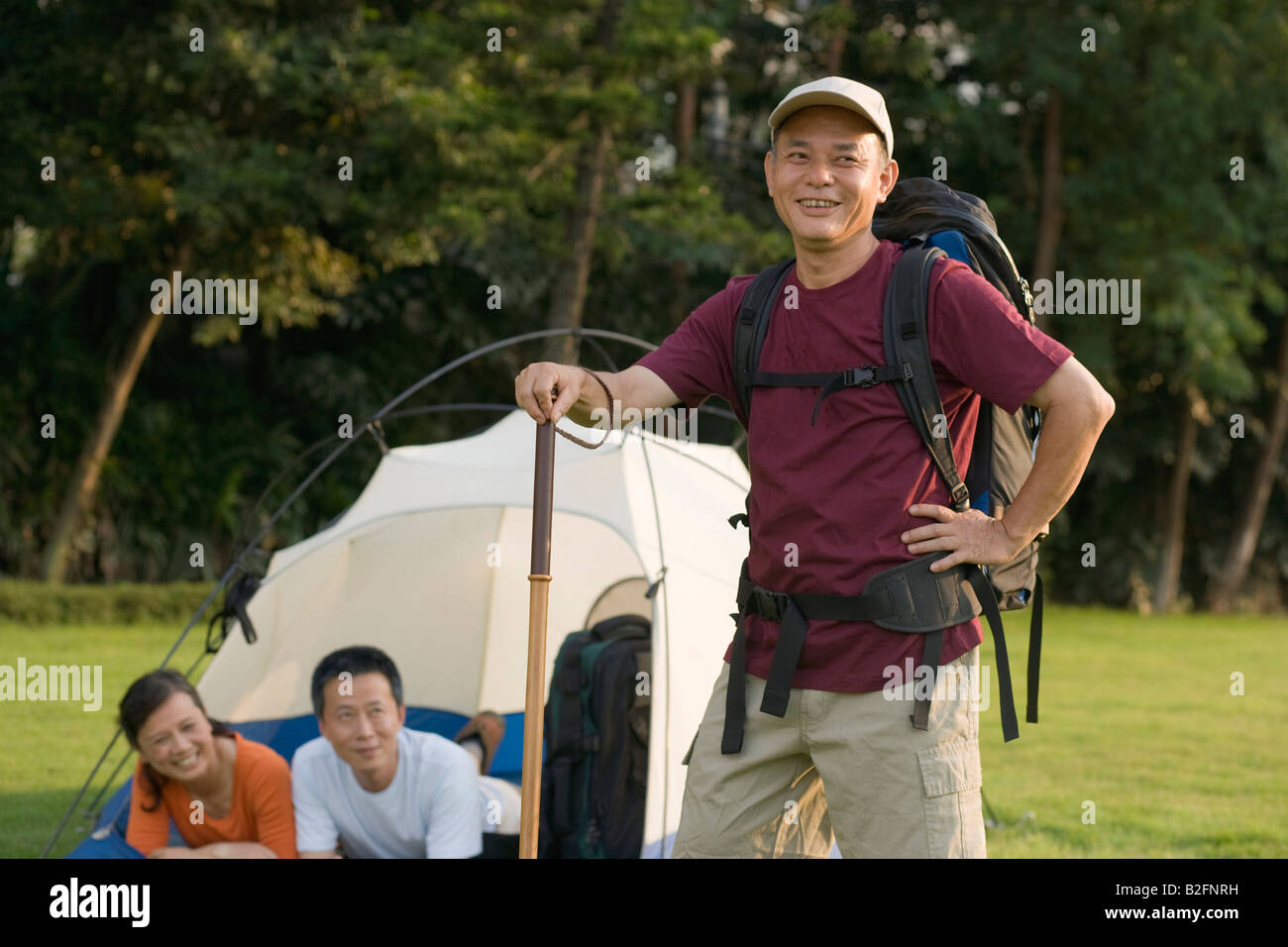 Mature man holding a hiking pole and his friends resting in the tent Stock Photo