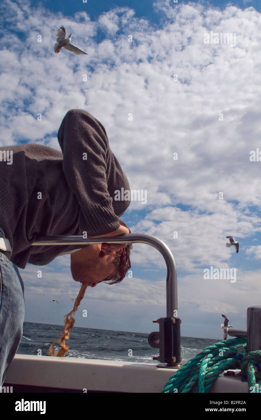 young man is sick over the side of a boat, while sea gulls fly overhead