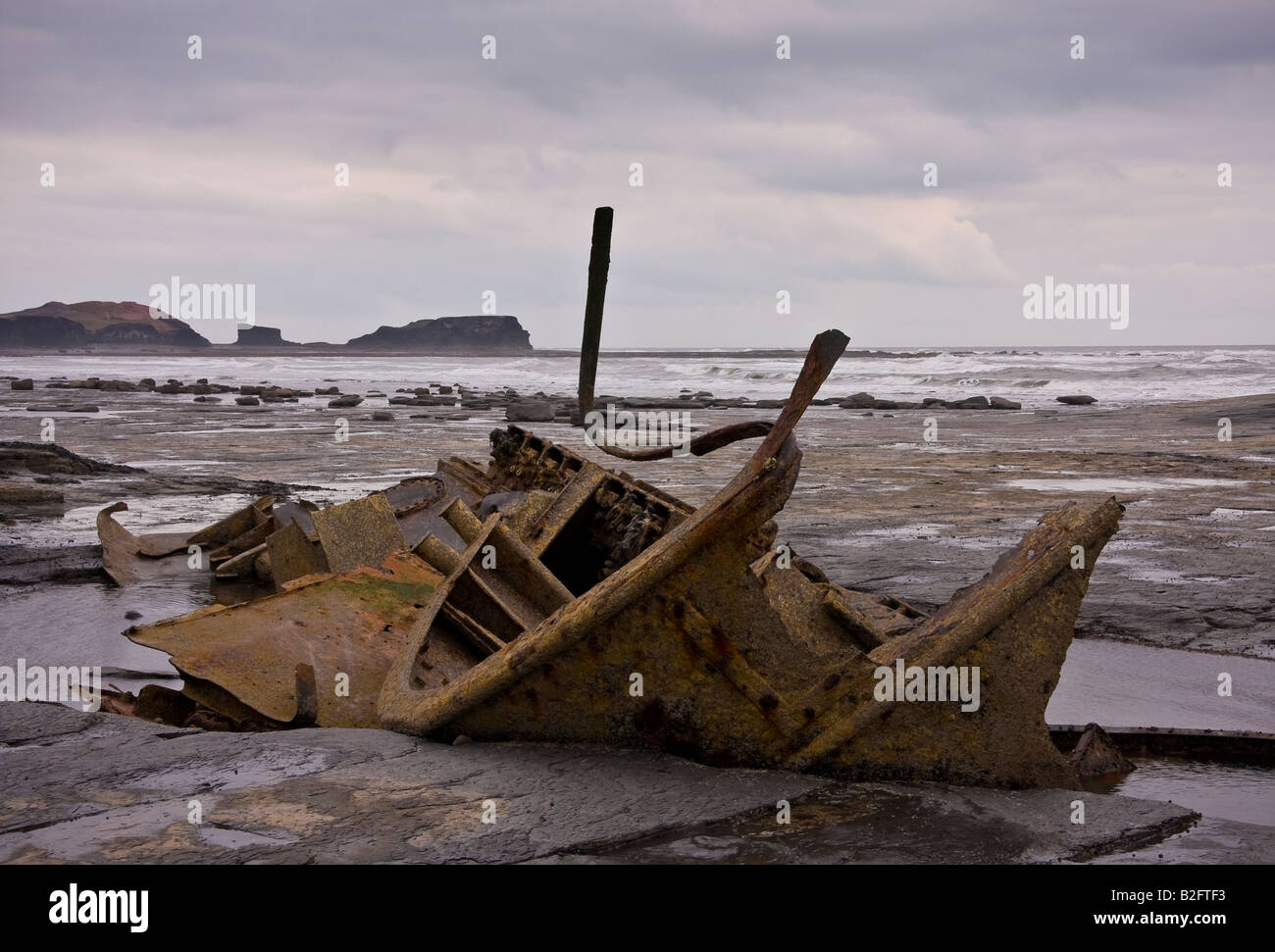 Old shipwreck on rocky shore at low tide with moody skies Stock Photo