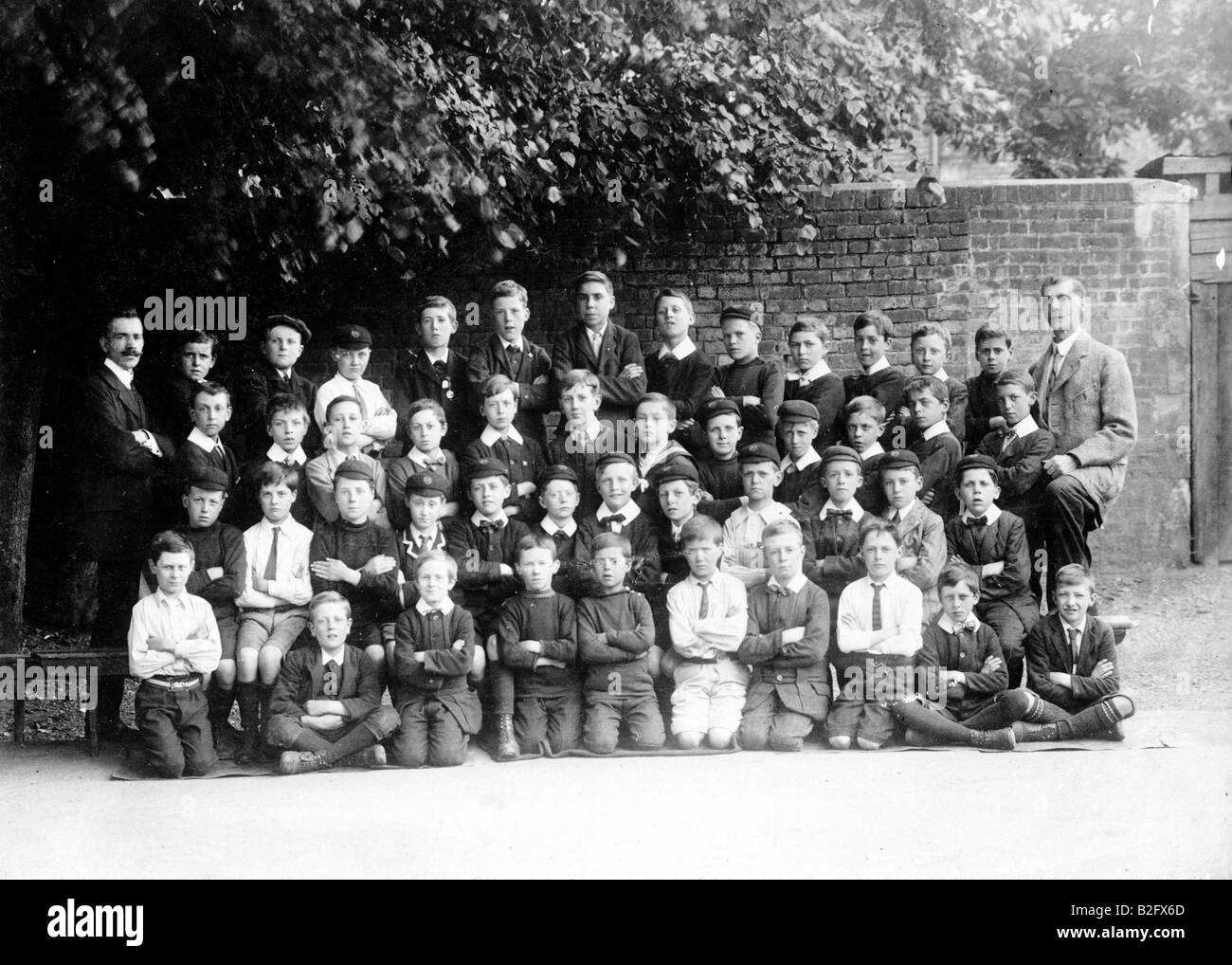 1906 black and white photograph of a class of pupils at the British School in Croydon, posing outdoors by a brick wall in four rows with two teachers. Stock Photo
