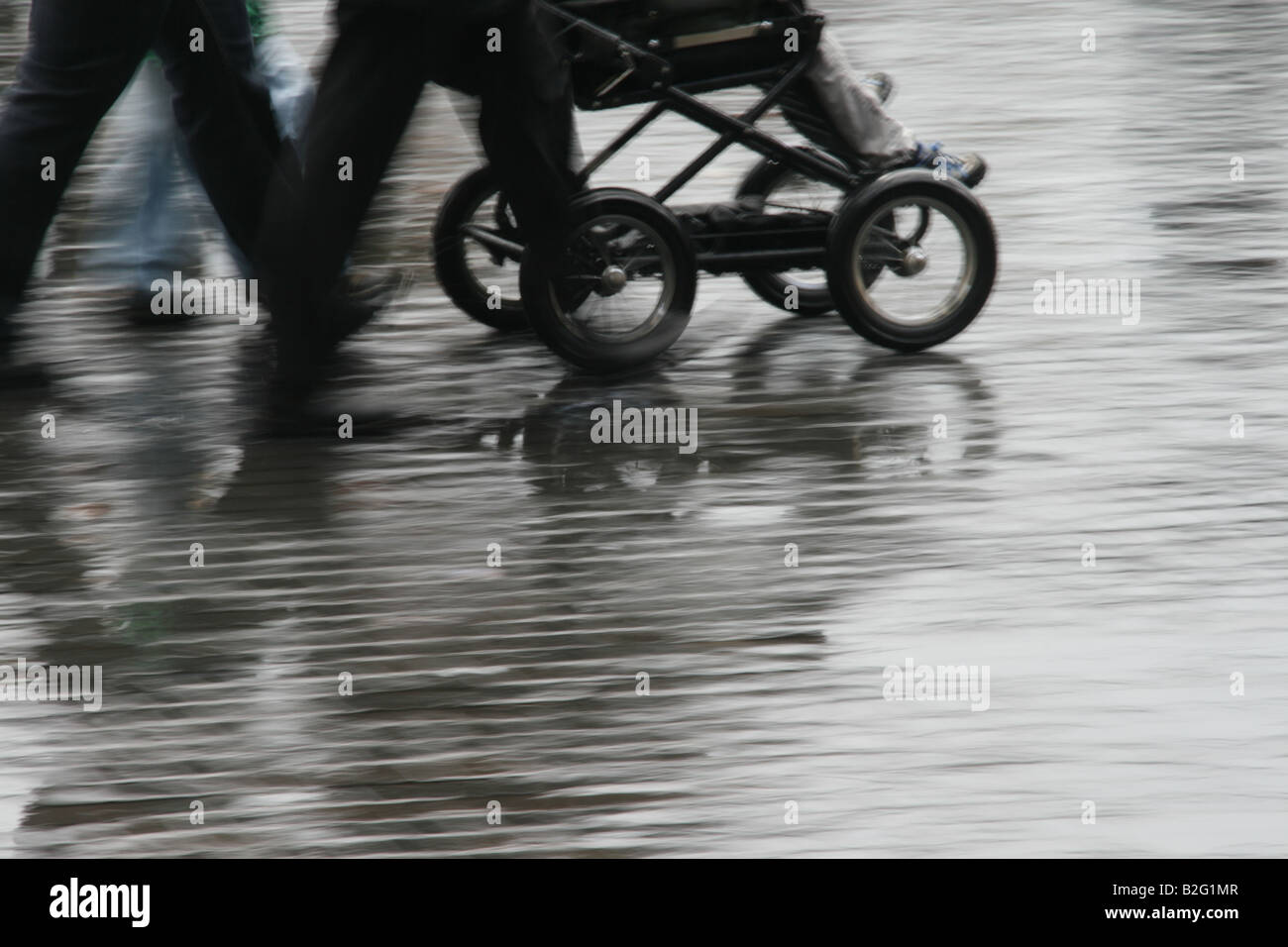 People Pushing Pram In Street In Rain In City Town Stock Photo