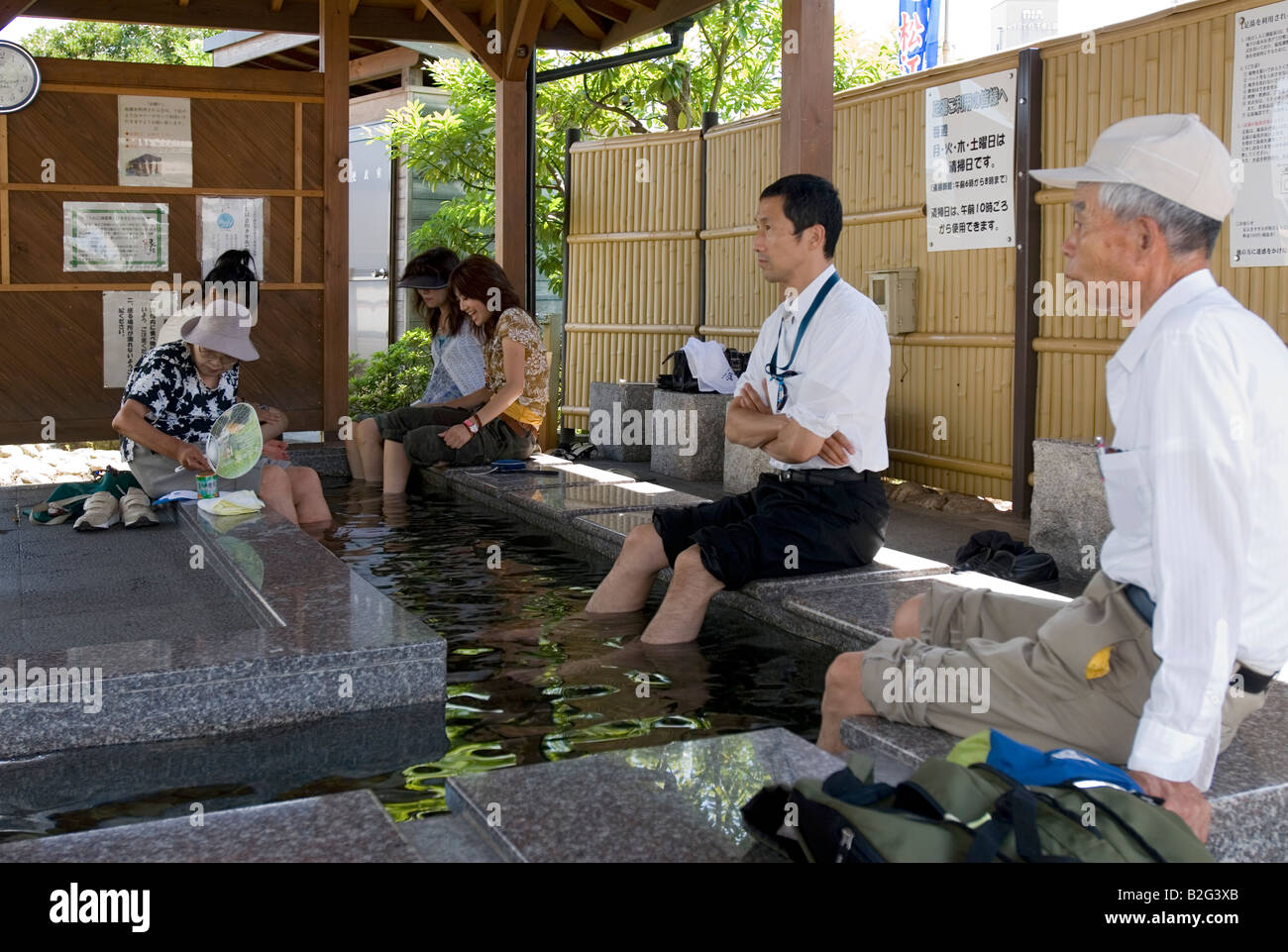 People relaxing with their feet immersed in a hot springs spa foot bath available to the public for free in Matsue Japan Stock Photo