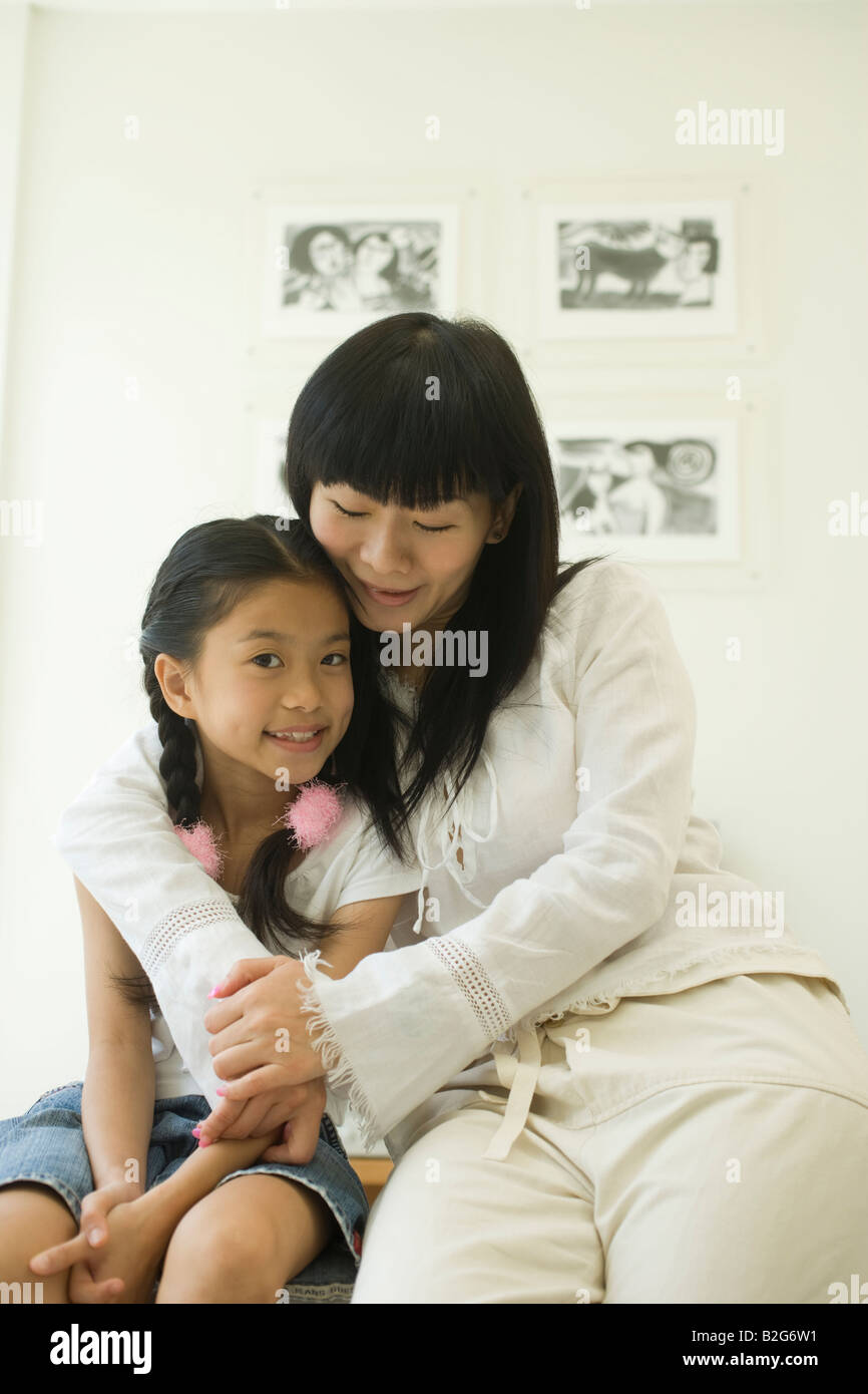 Mid adult woman sitting with arm around her daughter and smiling Stock Photo