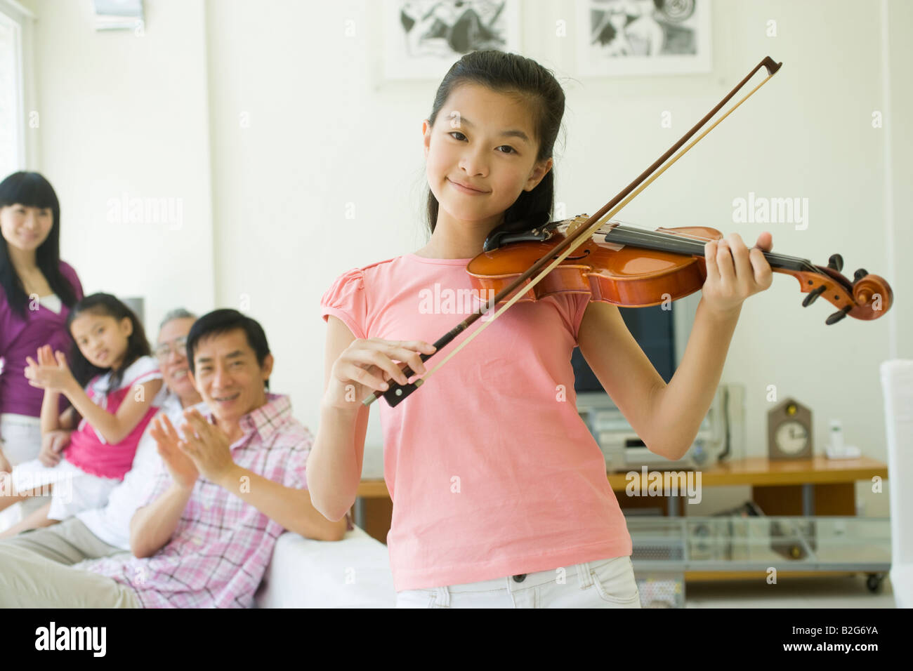 Girl playing a violin with her family applauding in the background Stock Photo
