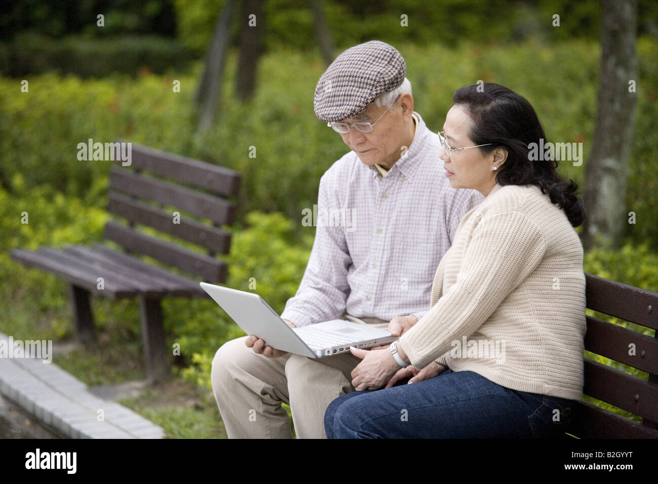 Senior couple sitting on a park bench and using a laptop Stock Photo ...