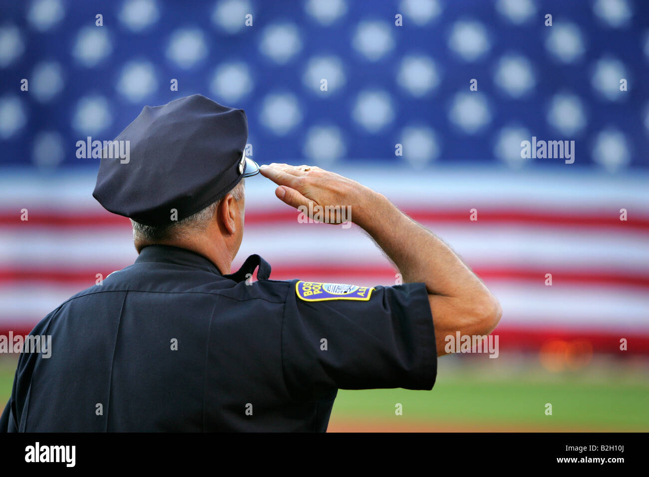 Police officer salutes giant flag baseball Fenway Park Stock Photo