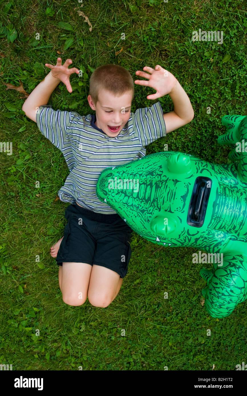 Young boy lying on the grass pretending that a plastic alligator is attacking him Model Released Stock Photo