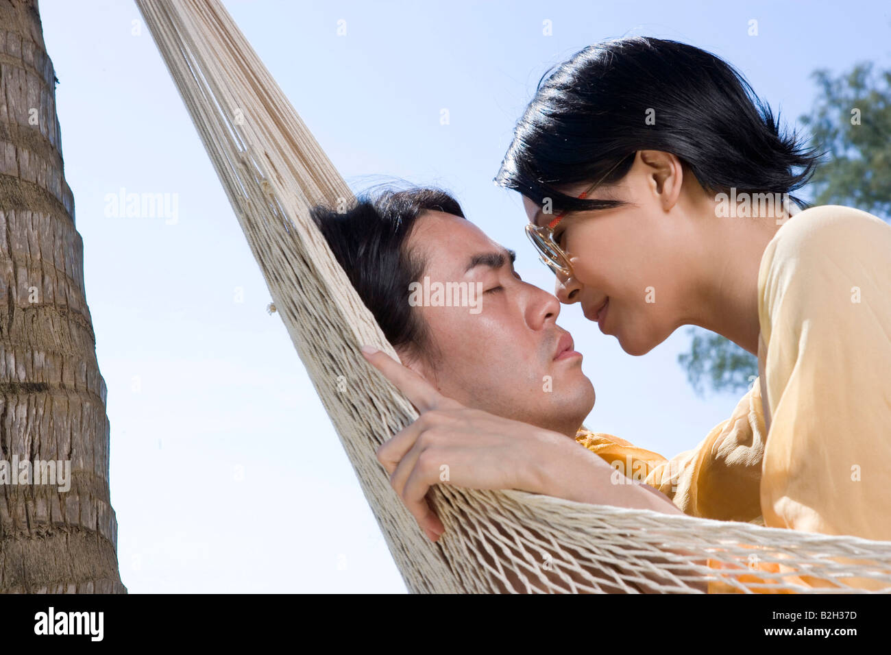 Side profile of a young woman kissing a young man reclining in a ...