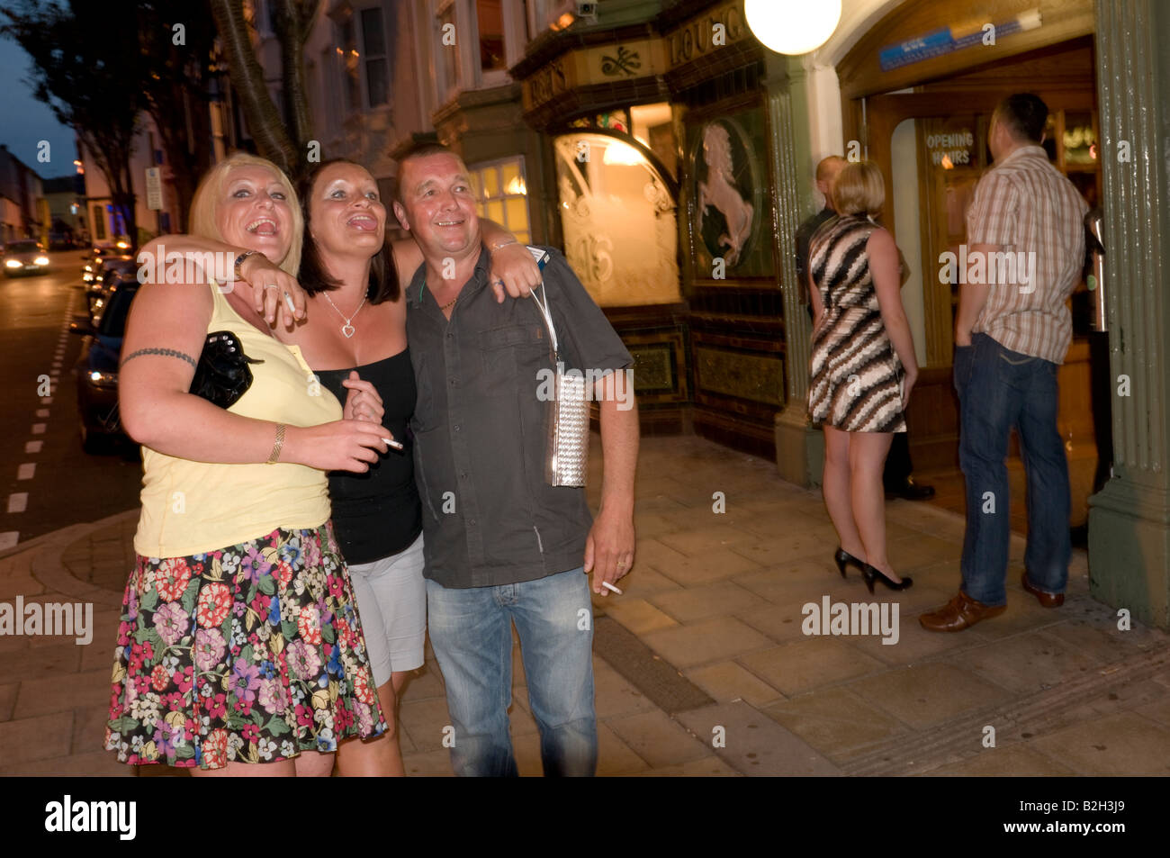 Three people man and two women outside pub smoking and posing for photograph in Aberystwyth Wales UK Stock Photo