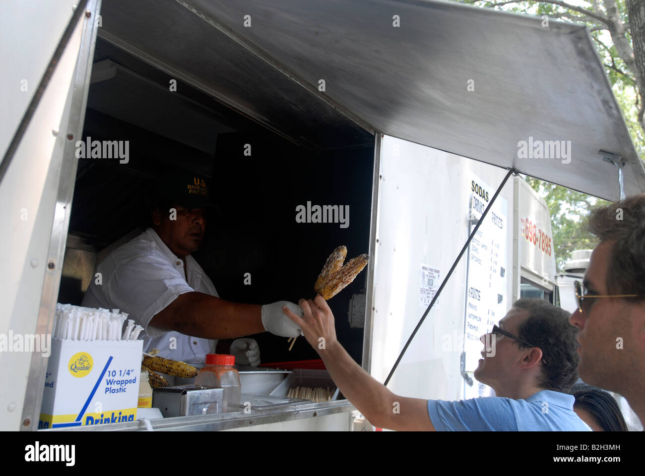 Customers are served Mexican style corn with a topping of mayo chili powder and cheese from a Latin food vendor Stock Photo