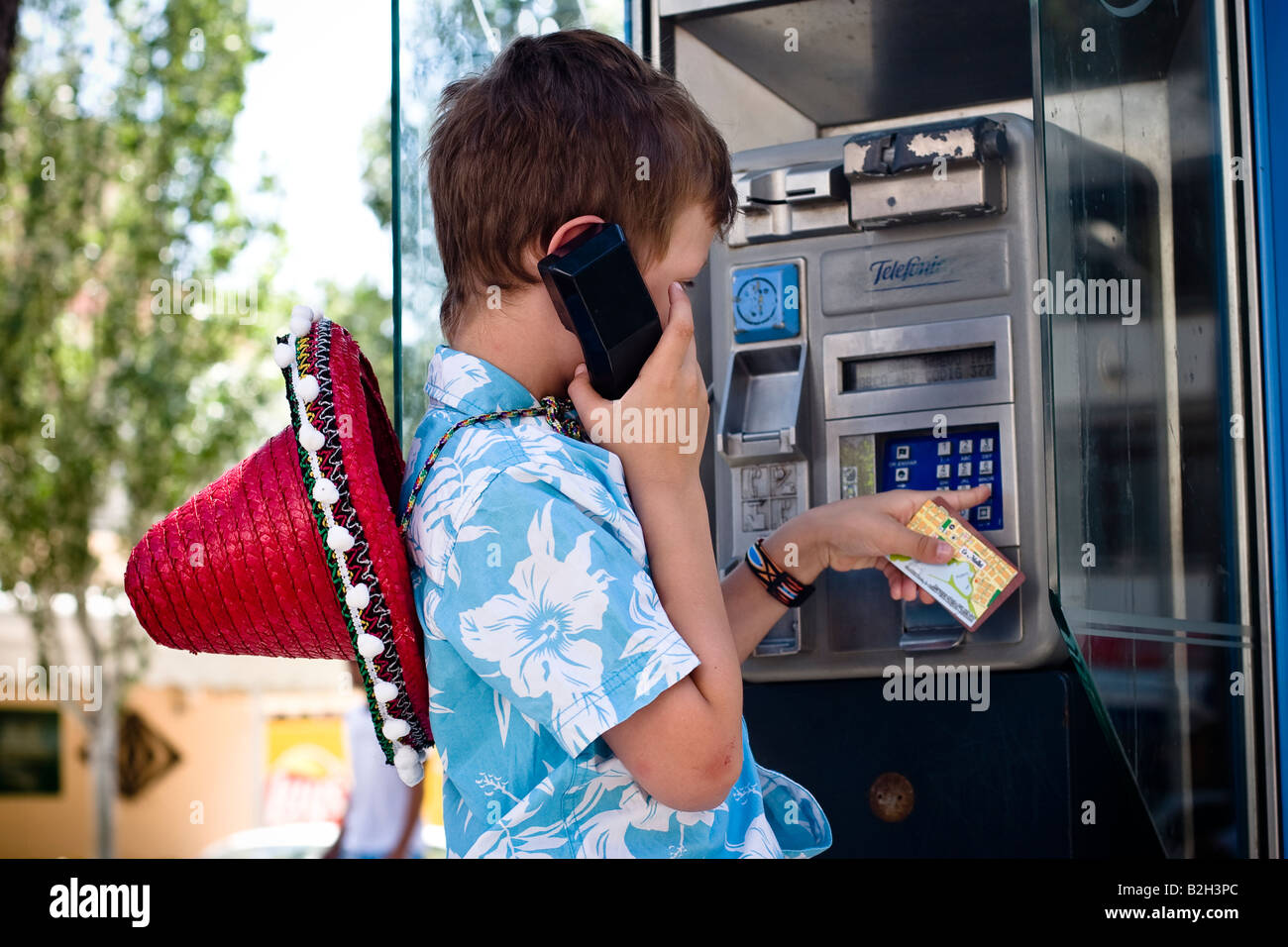 Young boy aged 7-8 makes phone call in public telephone box of the spanish telecom provider Telefonica in Cala Ratjada, Majorca Stock Photo
