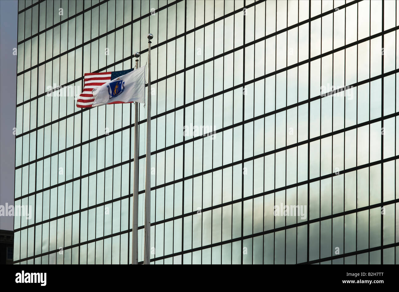 Massachusetts and American flags flying in front of reflective building Stock Photo