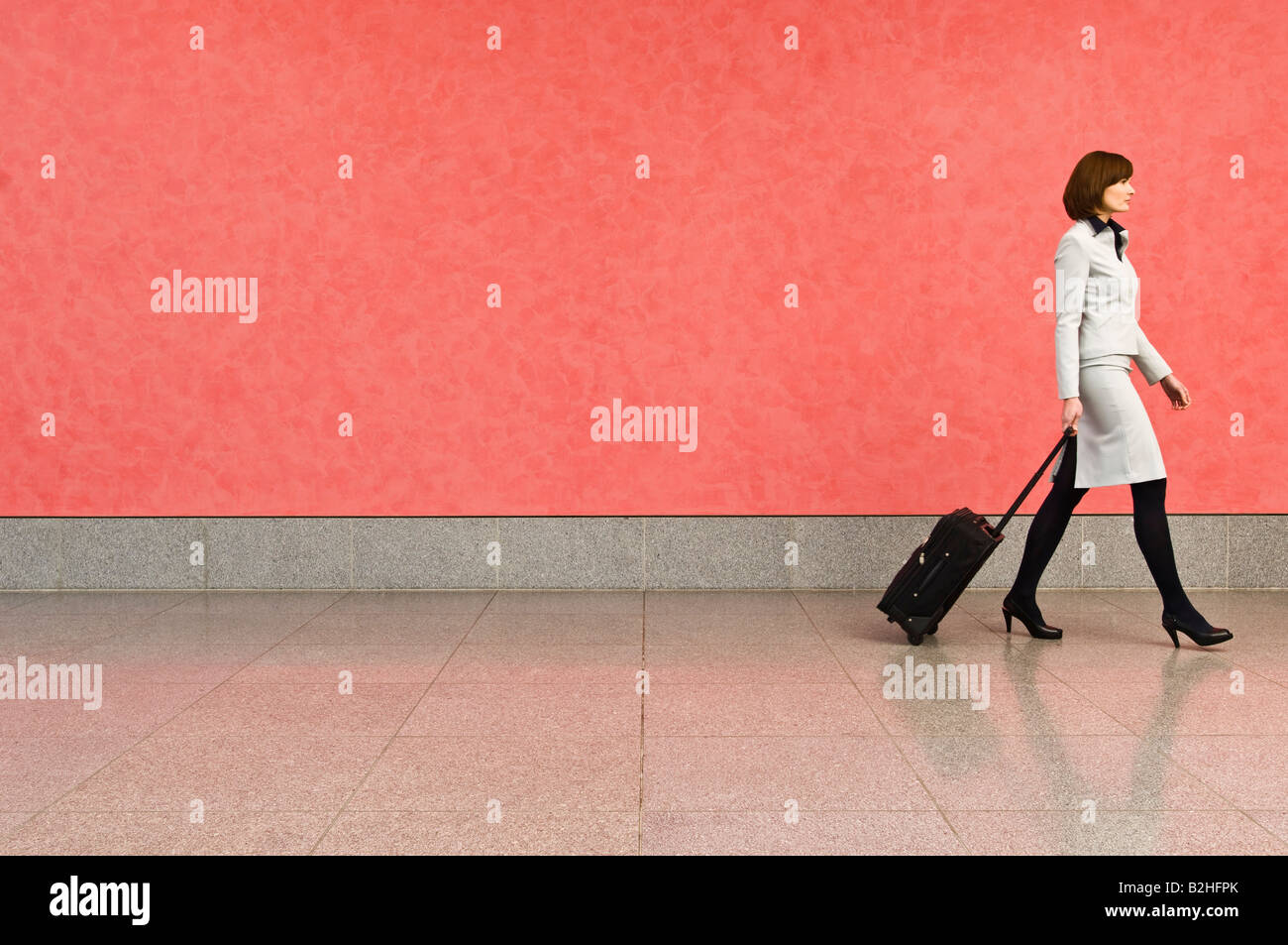businesswoman in corridor pulling carry-on suitcase Stock Photo