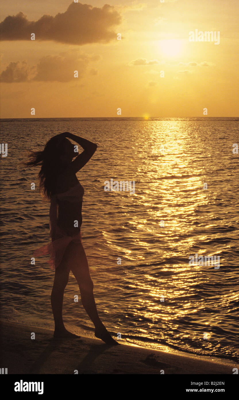 Silhouette of a woman standing on a beach at sunset. Stock Photo