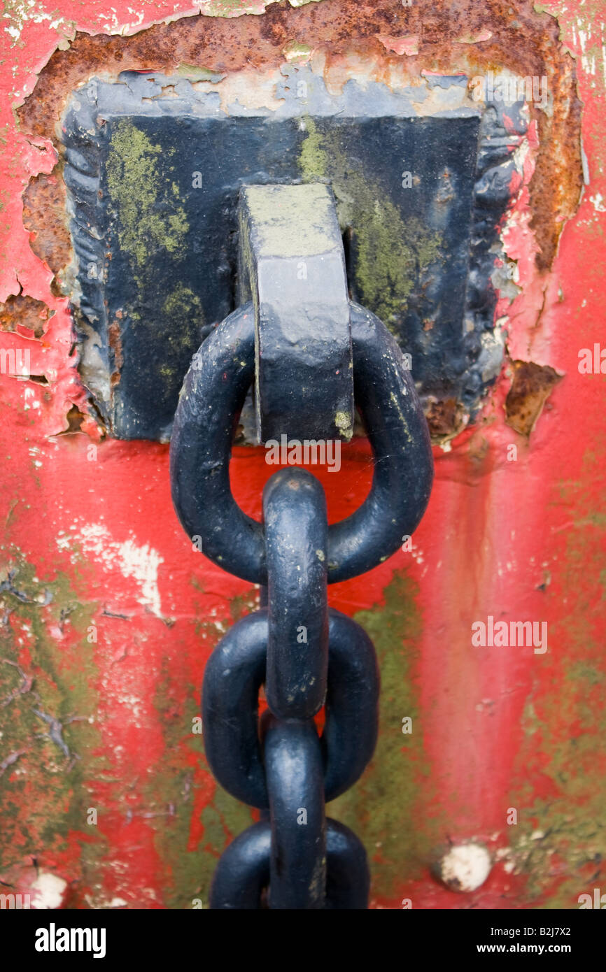 Painted black chain attached to a rusting red post Stock Photo - Alamy