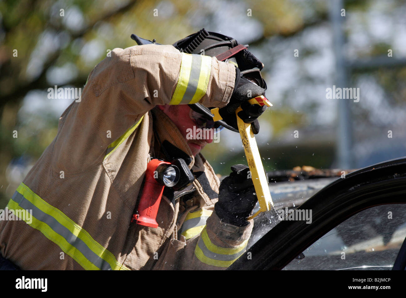 A firefighter using a Glass Master tool to cut the windshield of a car out during extrication of a victim Stock Photo