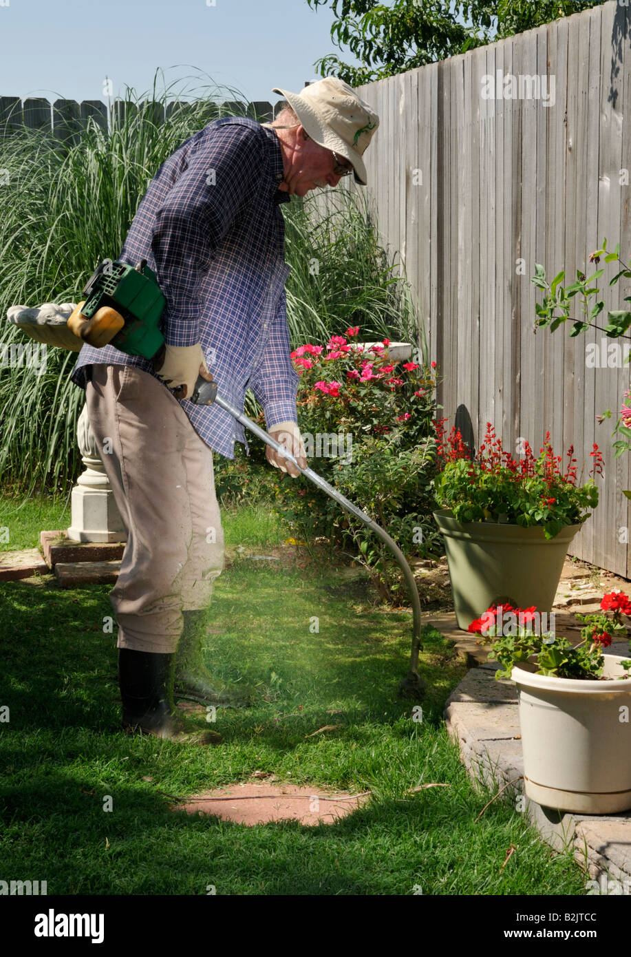 A 70 year old caucasian man uses a gasolinepowered weedeater to trim