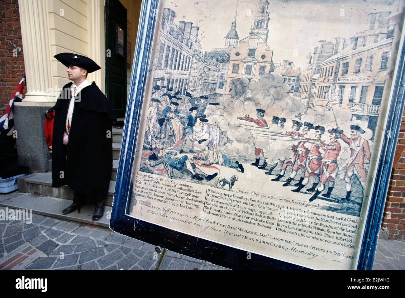 A reenactor in colonial era British army attire stands next to a period depiction of the Boston Massacre on the site it occurred Stock Photo