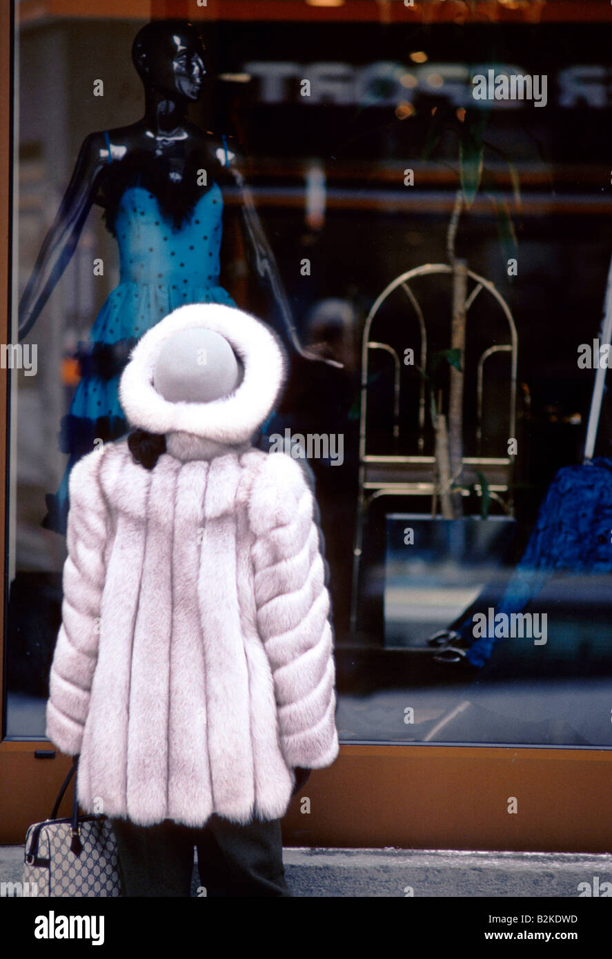 WOMAN WEARING FUR HAT COAT LOOKING AT DRESS DISPLAYED ON MANNEQUIN IN SHOP WINDOW ST MORITZ Stock Photo