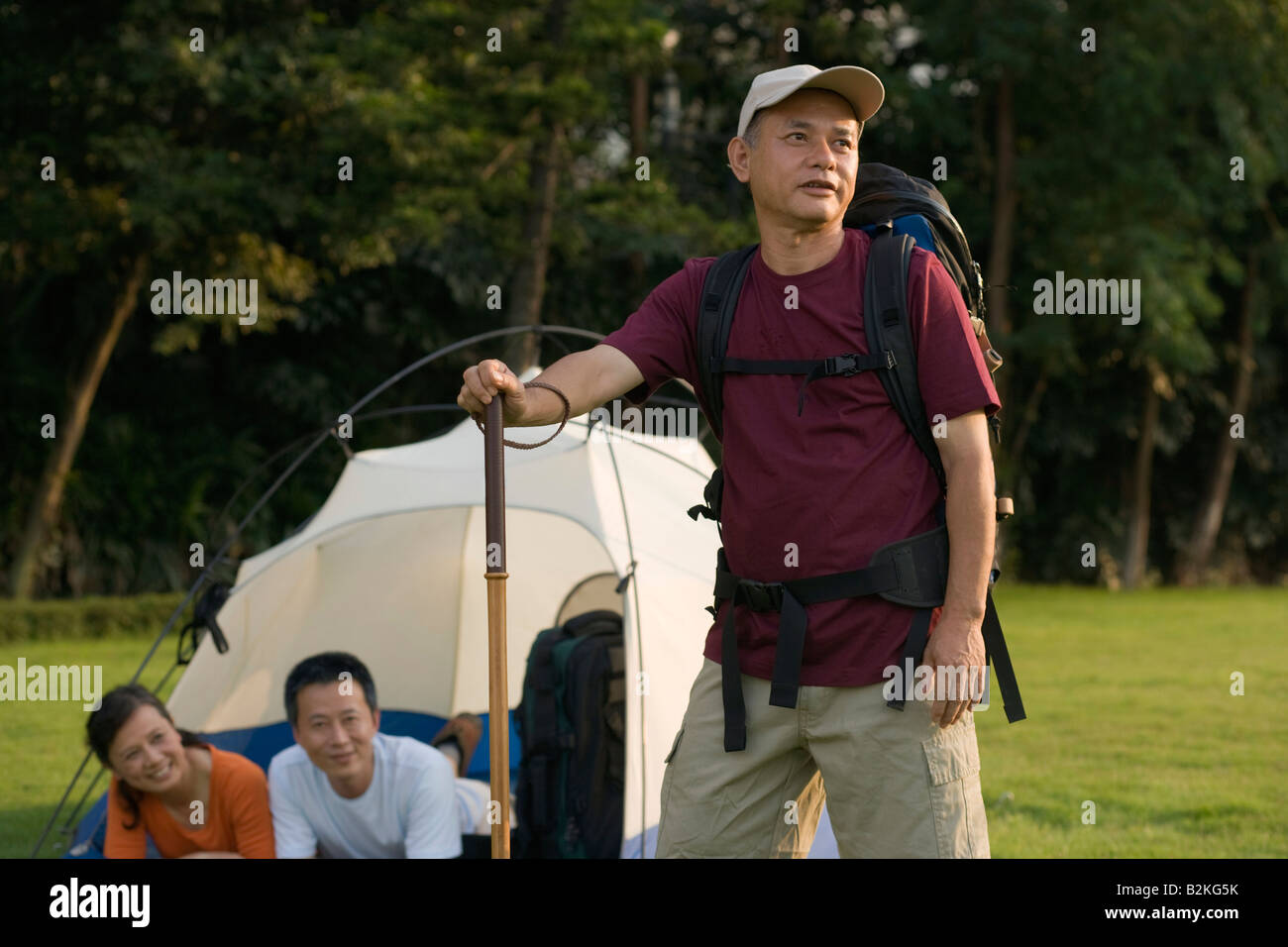 Mature man holding a hiking pole and his friends resting in the tent Stock Photo