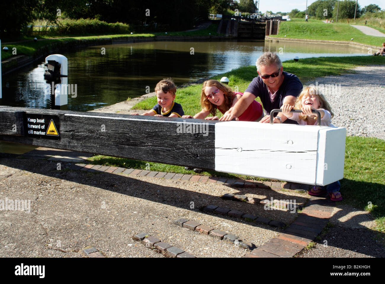 Children on a boating holiday push open lock gate Grand Union Canal England with the help of their father Stock Photo