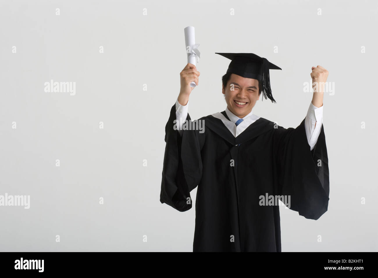 Portrait of a young male graduate holding a diploma with his arms ...
