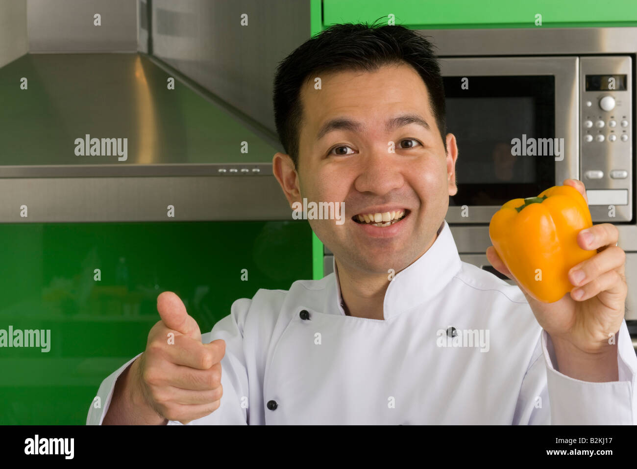 Portrait of a male chef holding a yellow bell pepper and showing a thumbs up sign Stock Photo