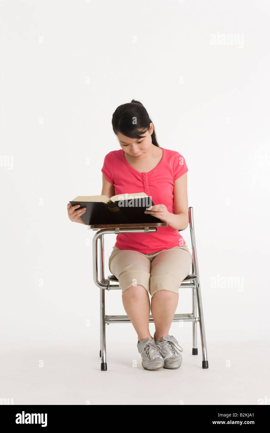 Young woman sitting on a writing chair and reading a book Stock Photo ...
