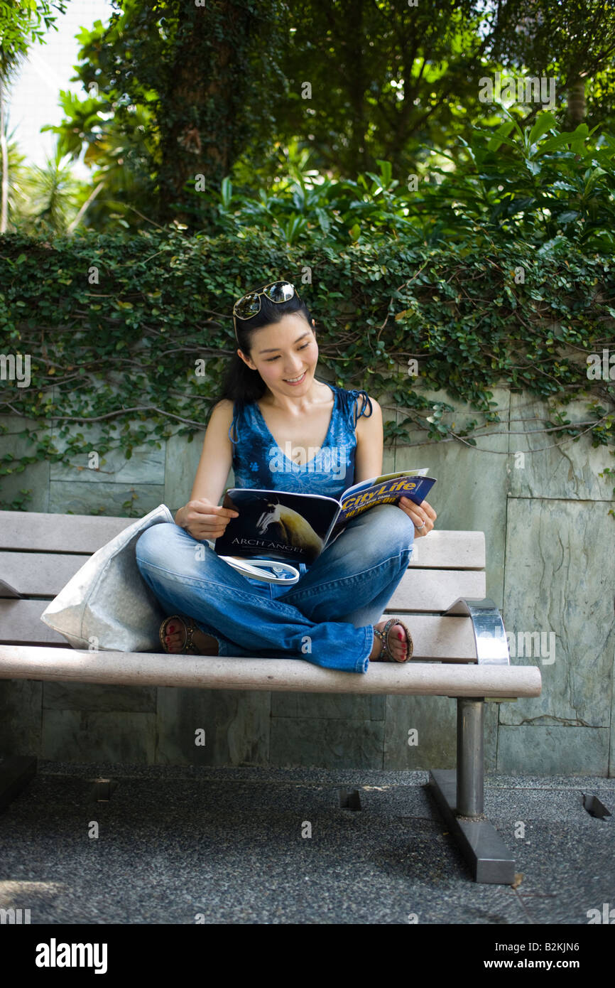 Young woman sitting on a bench in a park and reading a magazine Stock ...