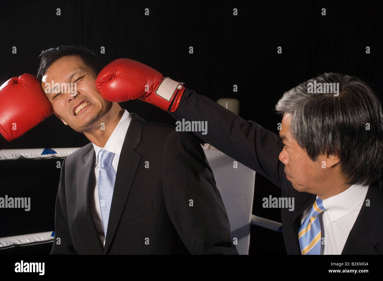 Businessman being hit by his two opponents in a boxing ring Stock Photo