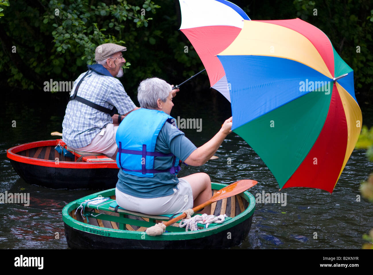 A man and a woman in coracles being propelled by the wind with an umbrella Stock Photo