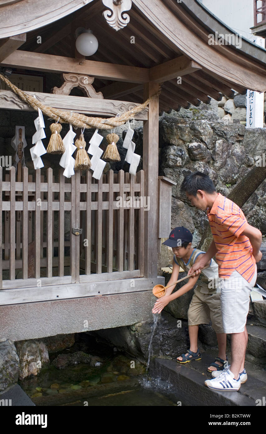In a Shinto purification ritual a man pours clean water on the hands of a boy standing before a shrine in Gujo Hachiman Stock Photo