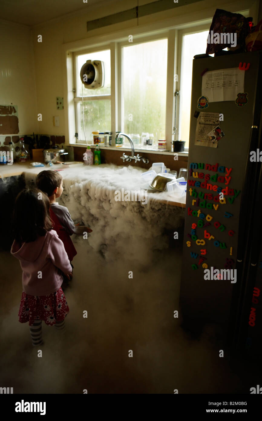 Boy aged six and sister five watch as dry ice boils in a kitchen sink full of water Stock Photo
