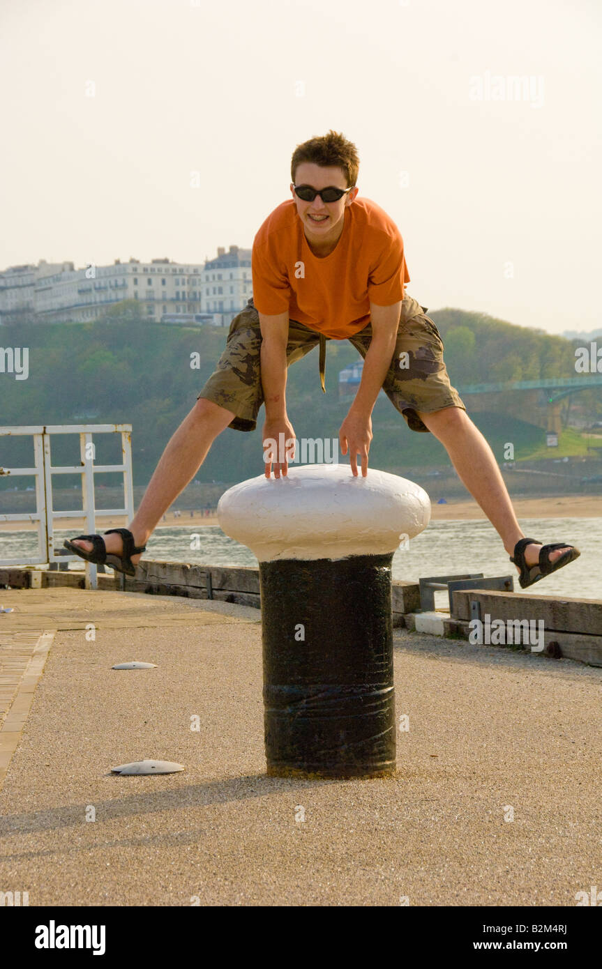 Caucasian teenage boy wearing short and t shirt, mid-air leapfrogging over a concrete mooring bollard in Scarborough harbour UK Stock Photo