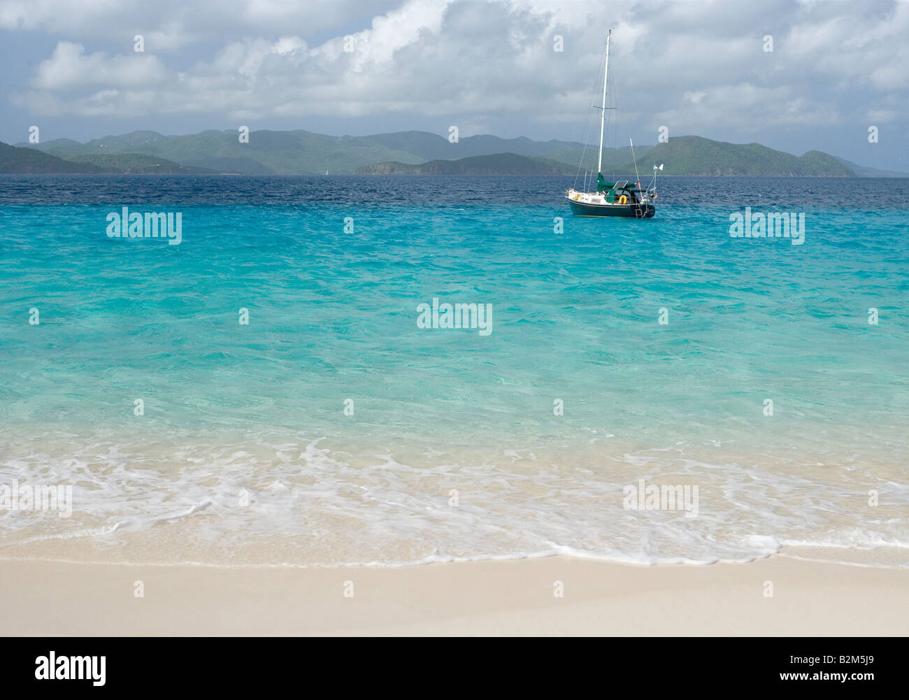 A cruising sailboat anchored next to Sandy Cay in the British Virgin Islands St John is visible in the background Stock Photo