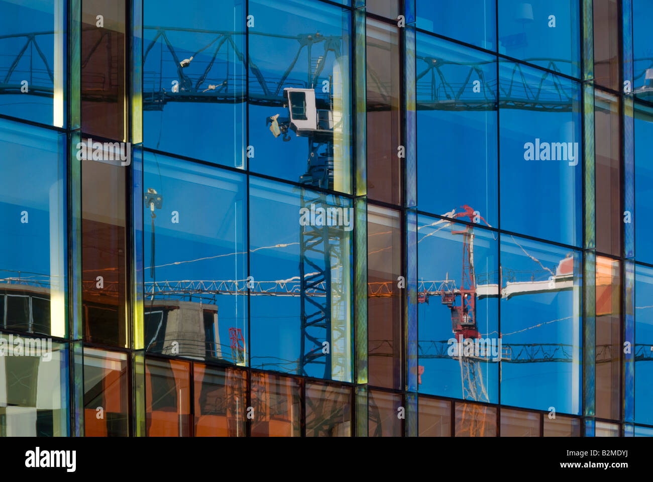 Building Cranes Reflected on the Gleaming Glass Facade of New Office Blocks Stock Photo