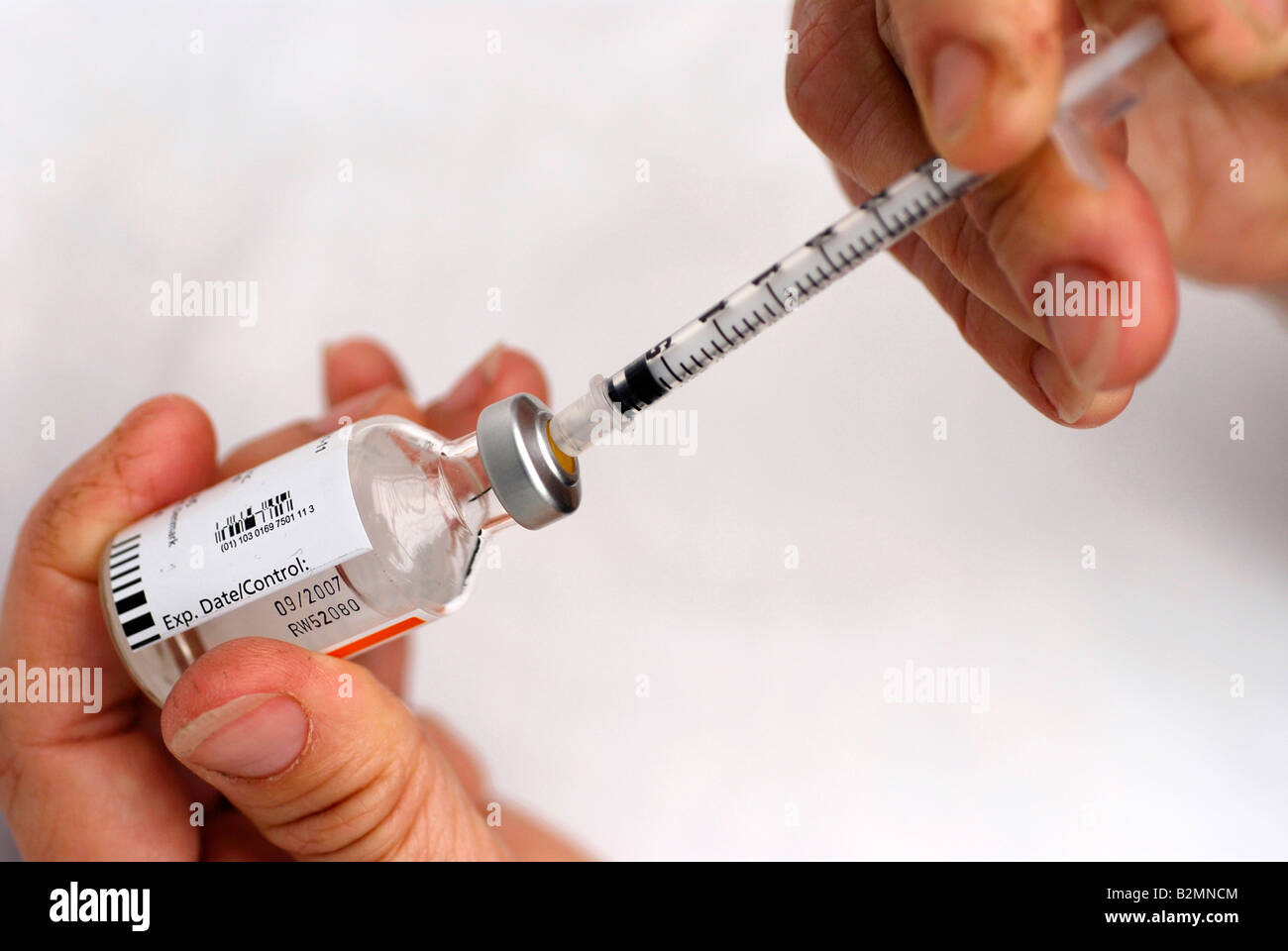 Diabetic inserting hypodermic syringe needle into insulin bottle cap