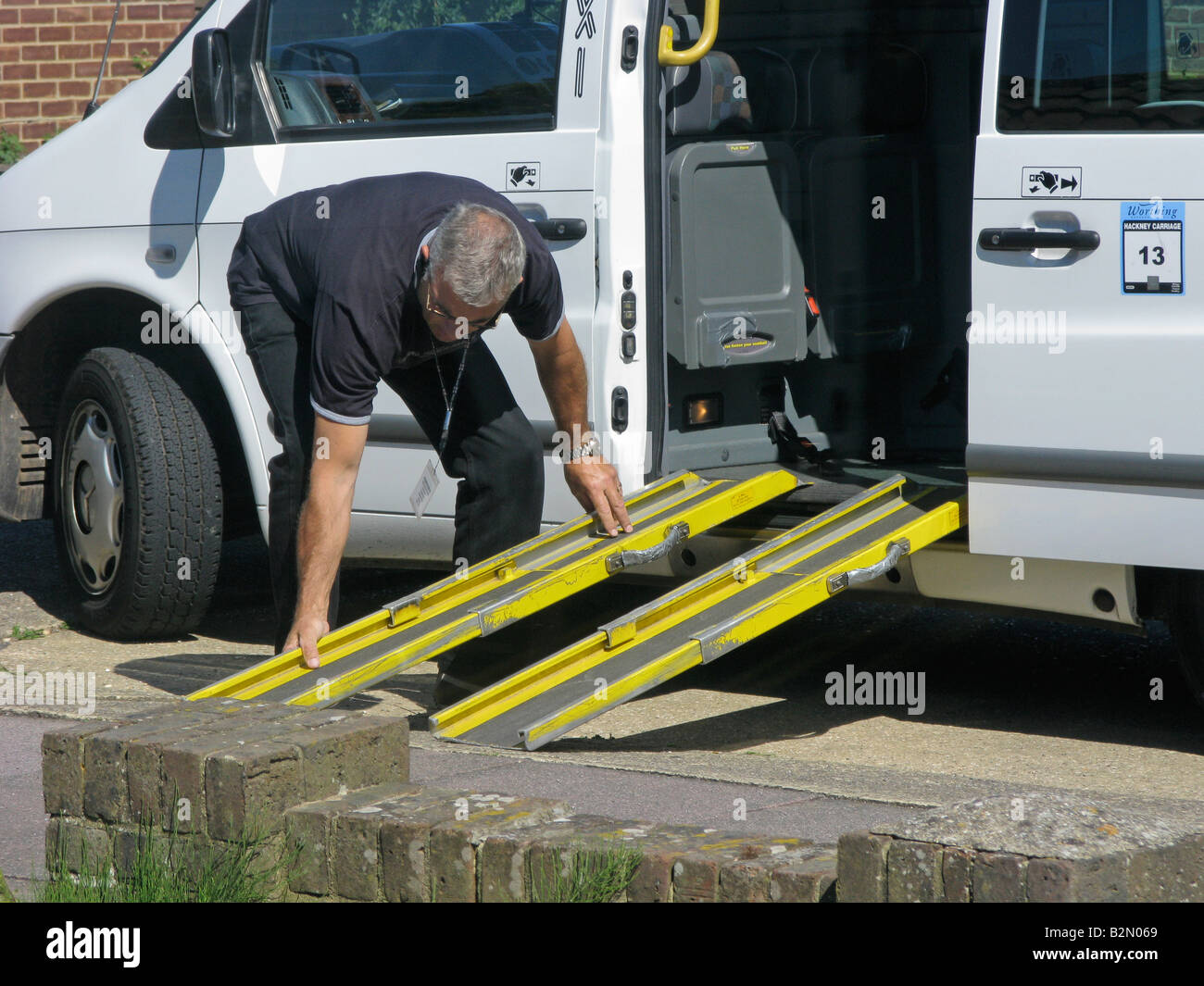 taxi driver putting a two piece slip resistant ramp into place to a wheelchair friendly taxi for the disabled enabling mobility Stock Photo