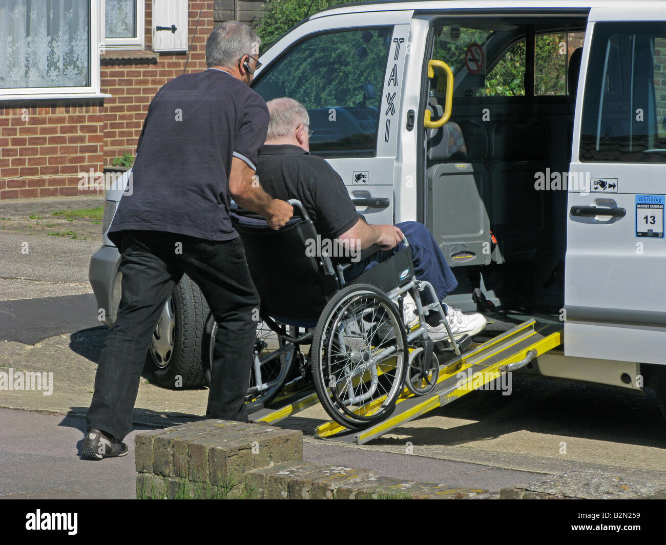 taxi driver pushing an elderly disabled man from a ramp to a wheelchair friendly taxi for the disabled enabling mobility Stock Photo