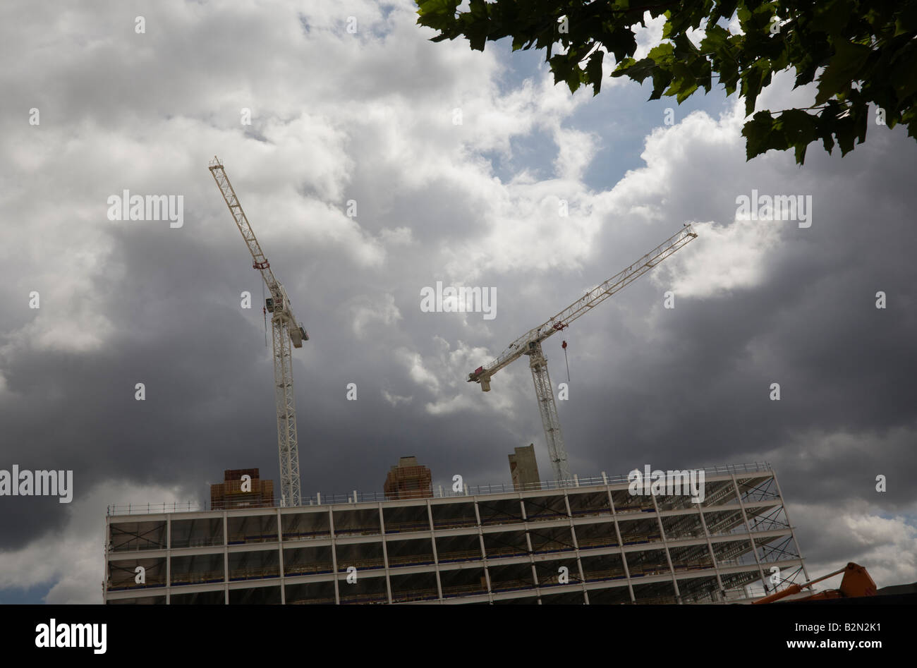Two construction cranes against dark grey clouds and sky Stock Photo