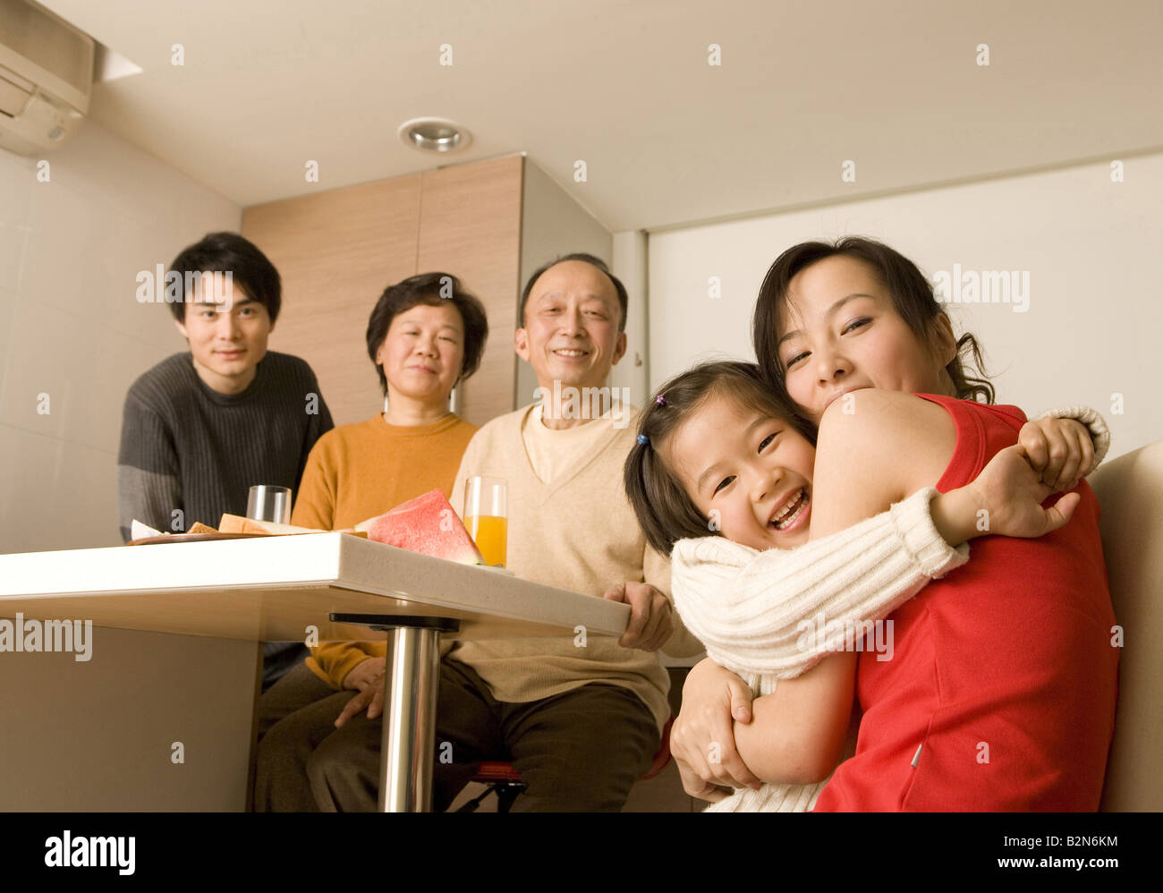 Portrait of a young woman hugging her daughter with her family members in the background Stock Photo